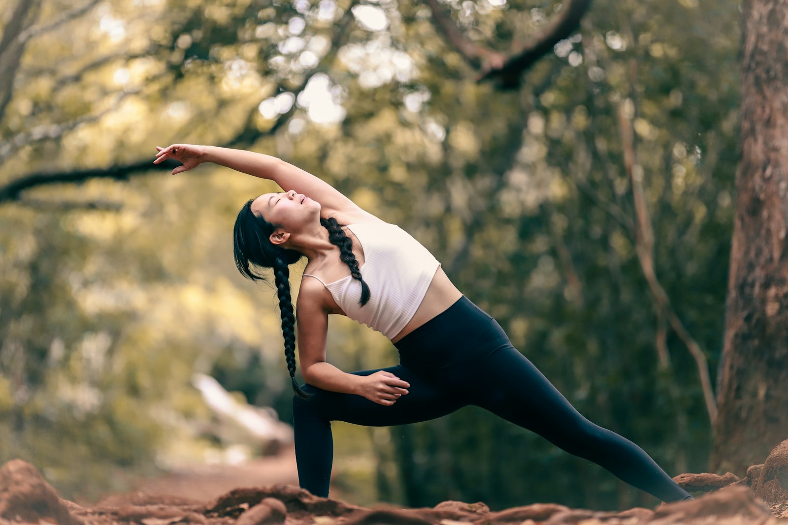 Woman doing a gentle yoga side stretch outdoors among trees